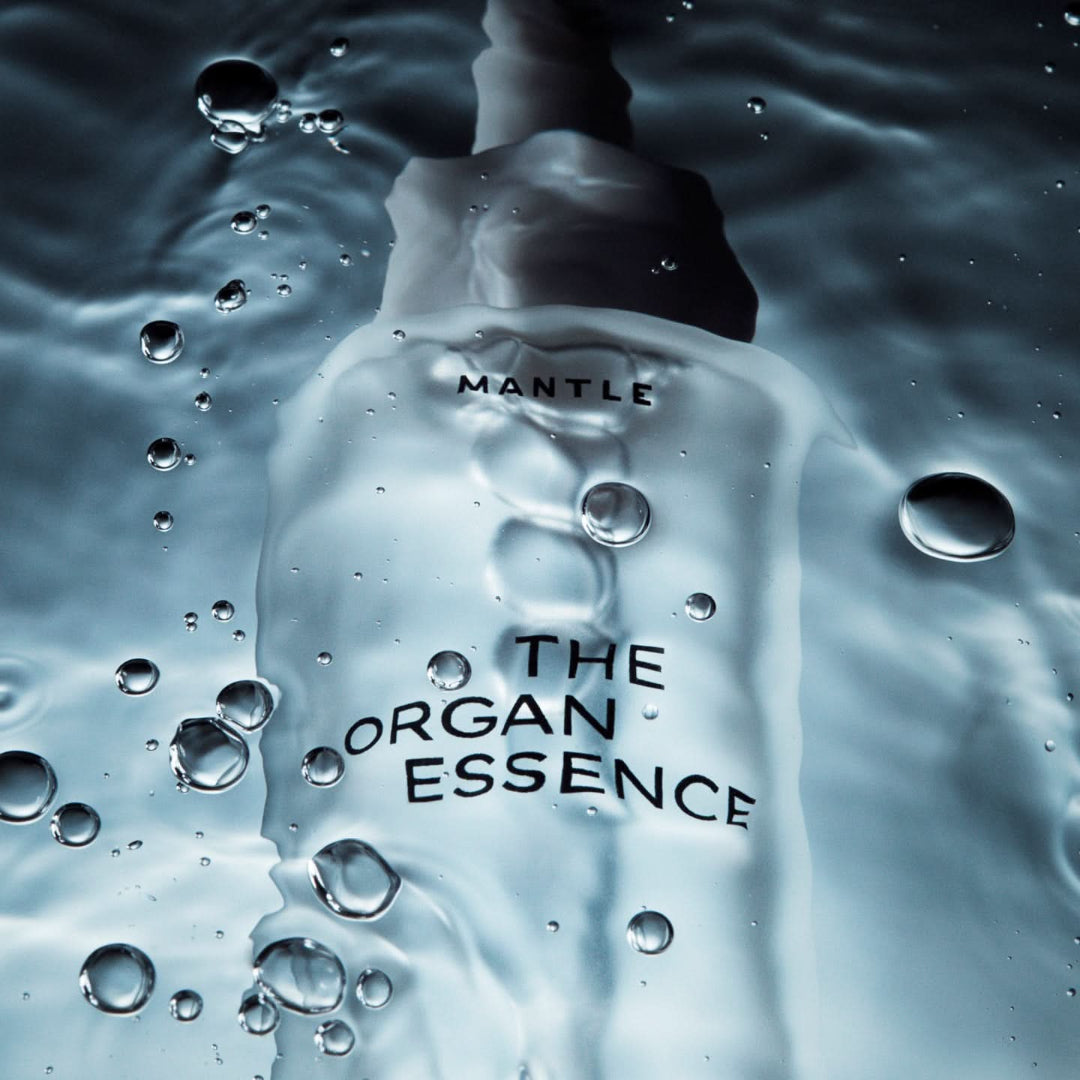 Bottle labeled 'MANTLE THE ORGAN ESSENCE' with water droplets on a reflective surface