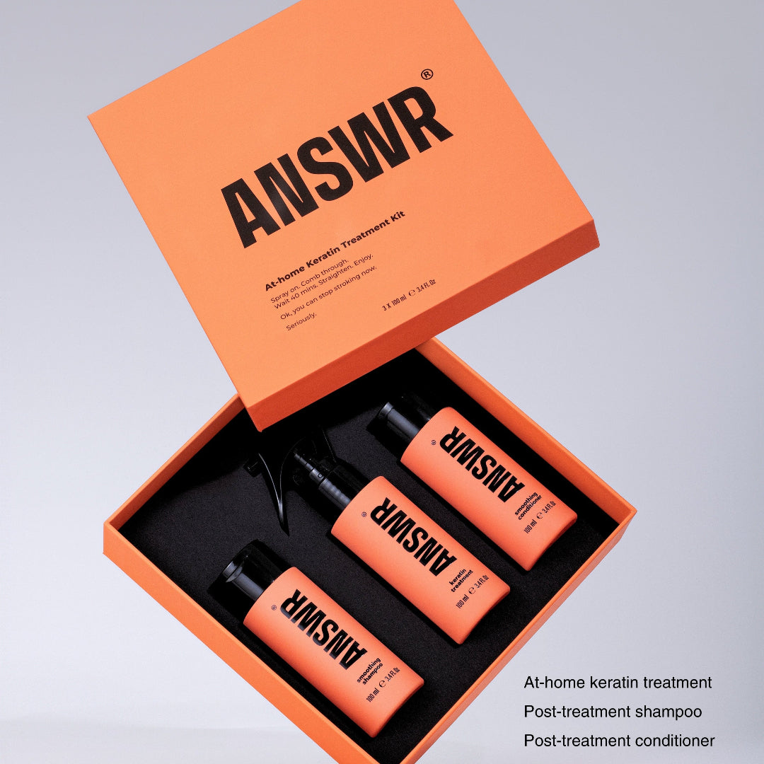 Orange 'ANSWR' hair care product set with bottles and a box on a light gray background.