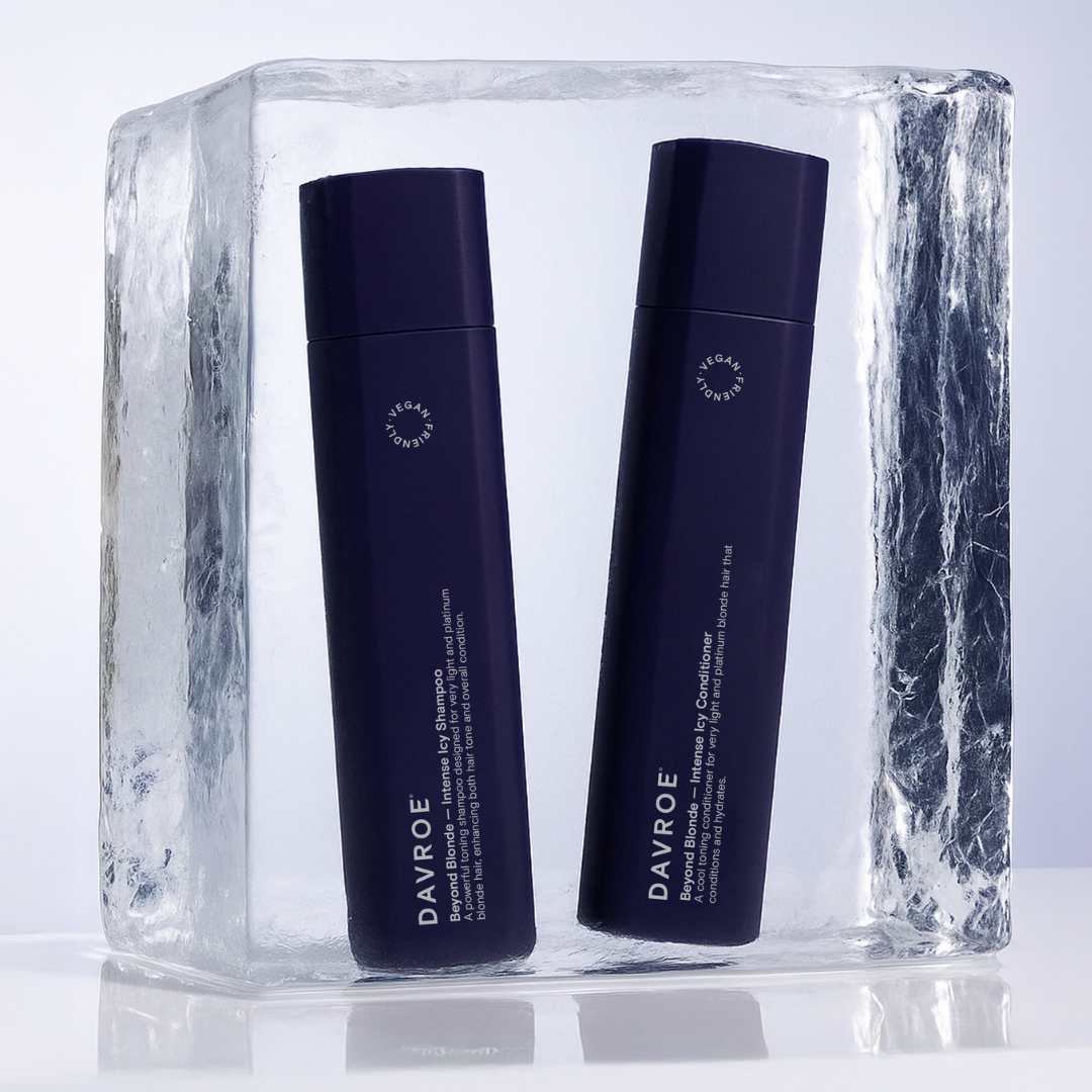 Two tall navy blue Davroe haircare bottles standing upright inside a clear ice block on a reflective white surface, with a light gray studio background.