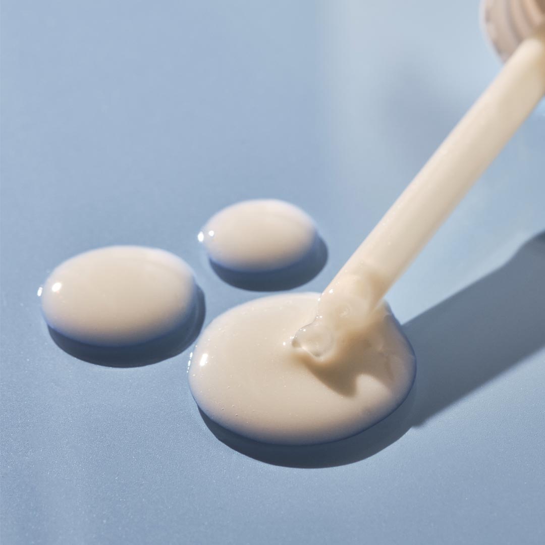 Beige cream being dripped from a spoon onto a blue background