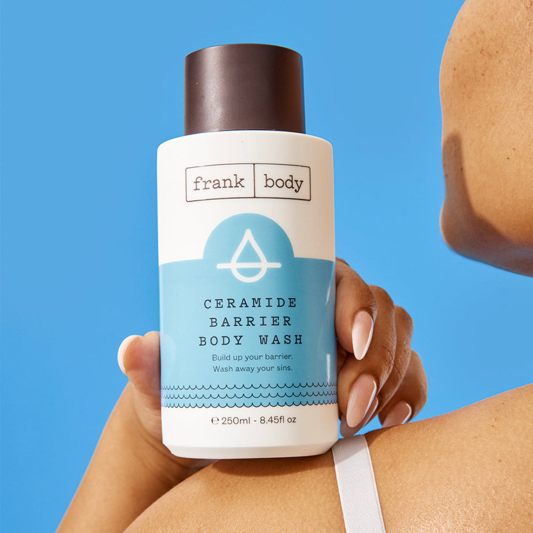 Person holding a bottle of frank body Ceramide Barrier Body Wash against a blue background