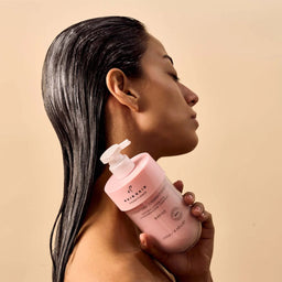 Woman holding a pink bottle of skincare product against a beige background