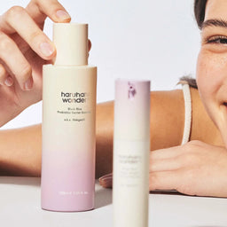 Two skincare bottles with a person holding one bottle in the background.