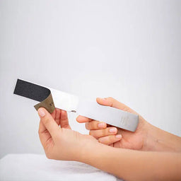 Hand holding a small electronic device with a black and gray component on a light gray background