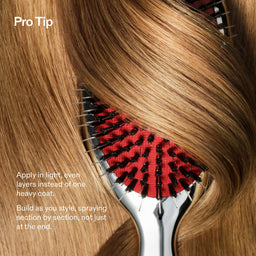 A close-up of a hairbrush with red bristle pads and black bristles, shown through layered light brown to blonde hair. White text on the left reads 'Pro Tip' and gives application instructions.