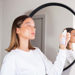 a women in front of a mirror applying Hello Sunday The Retouch One - Face Mist SPF30