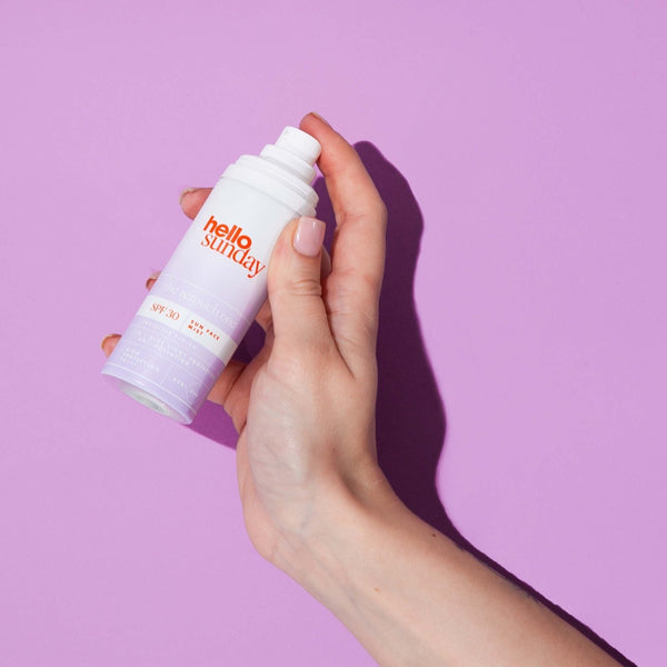 a hand holding Hello Sunday The Retouch One - Face Mist SPF30 on a purple surface